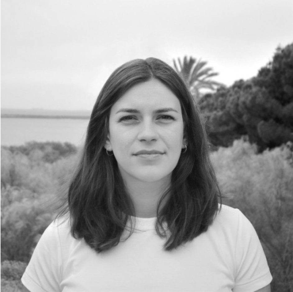 Black and white photo of a woman outdoors with trees and a body of water in the background.