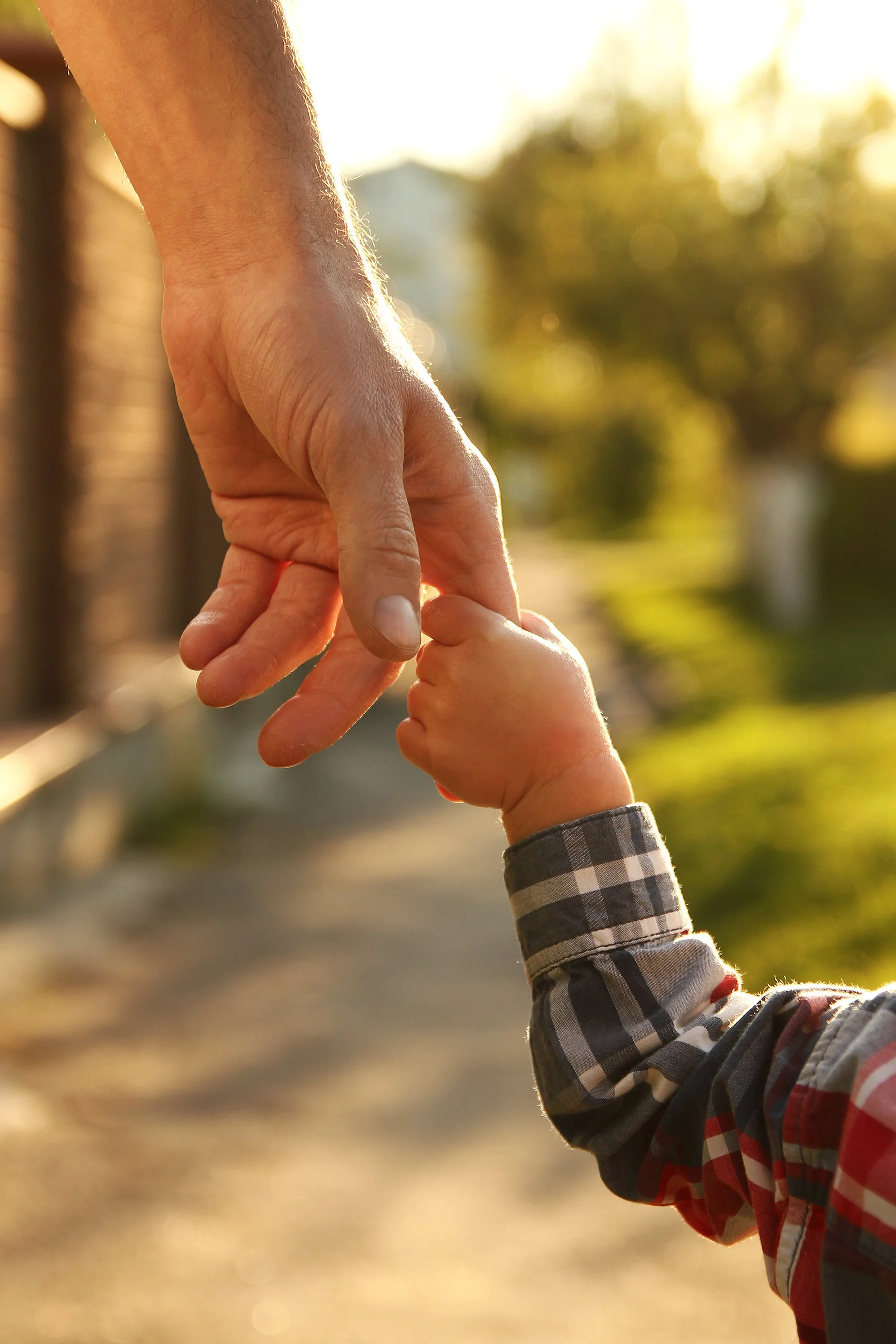 An adult hand gently holding a child's hand with sunlight in the background.
