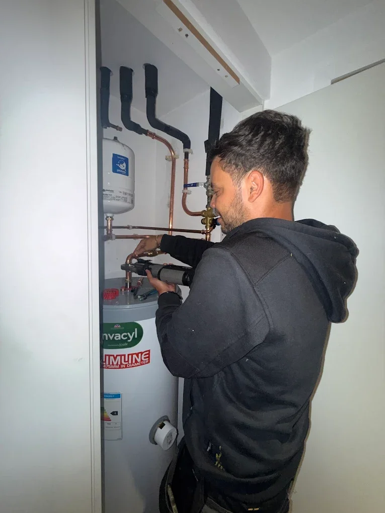 Man performing maintenance or repair on a water heater or boiler in a utility closet.