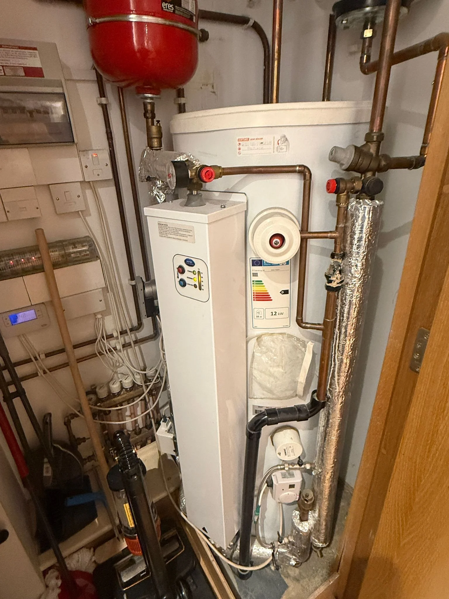 Closet with a water heater, copper pipes, gauges, and a red expansion tank.