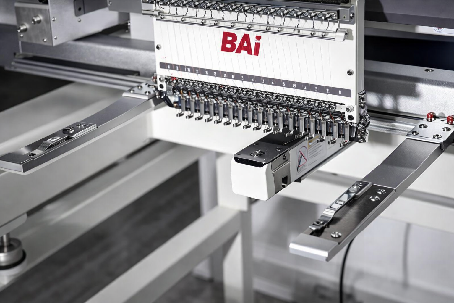 Close-up of industrial sewing machine with multiple needles and metal components, branded with the red text 'BAI'.