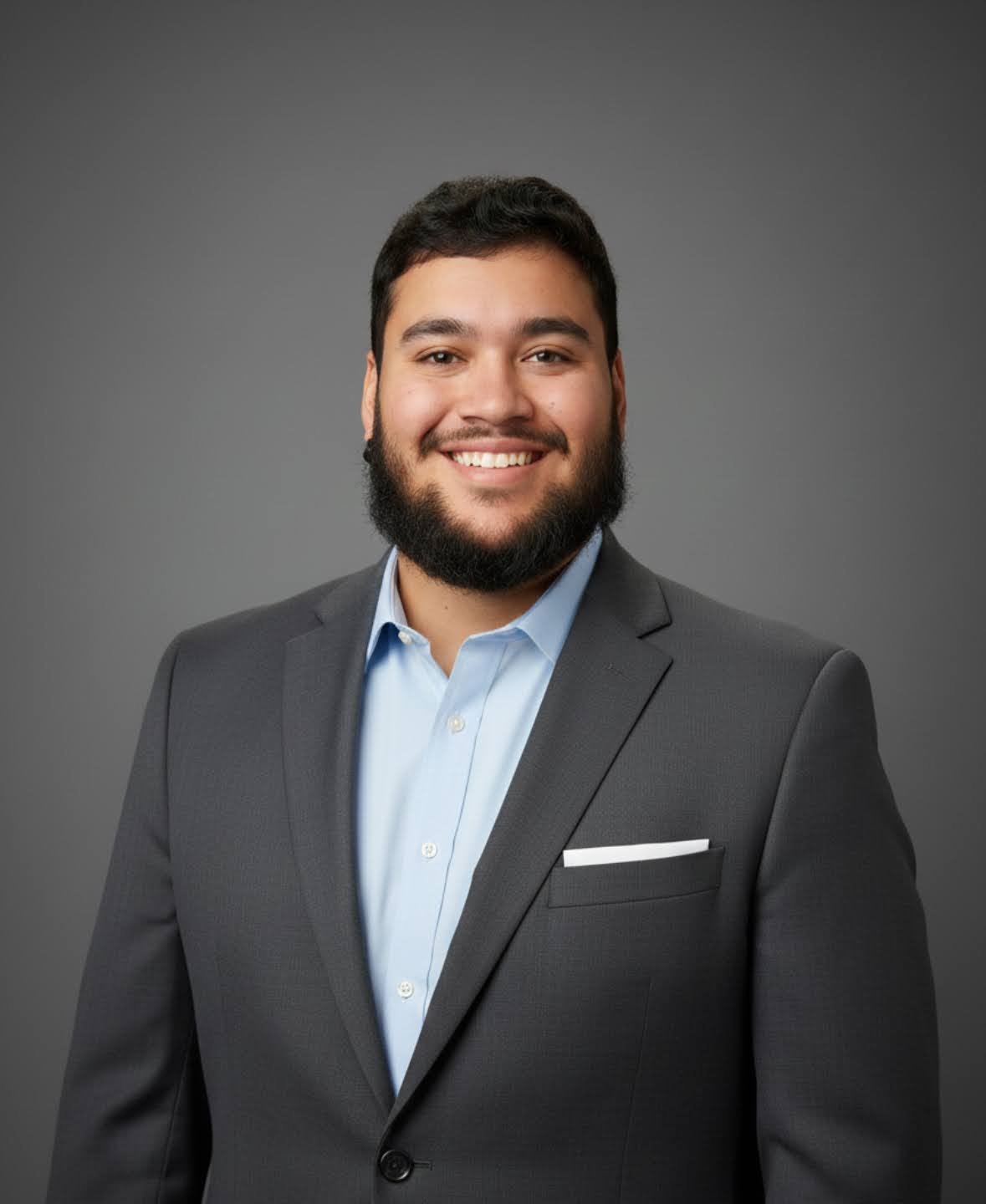 Dark haired bearded man wearing a gray suit jacket.