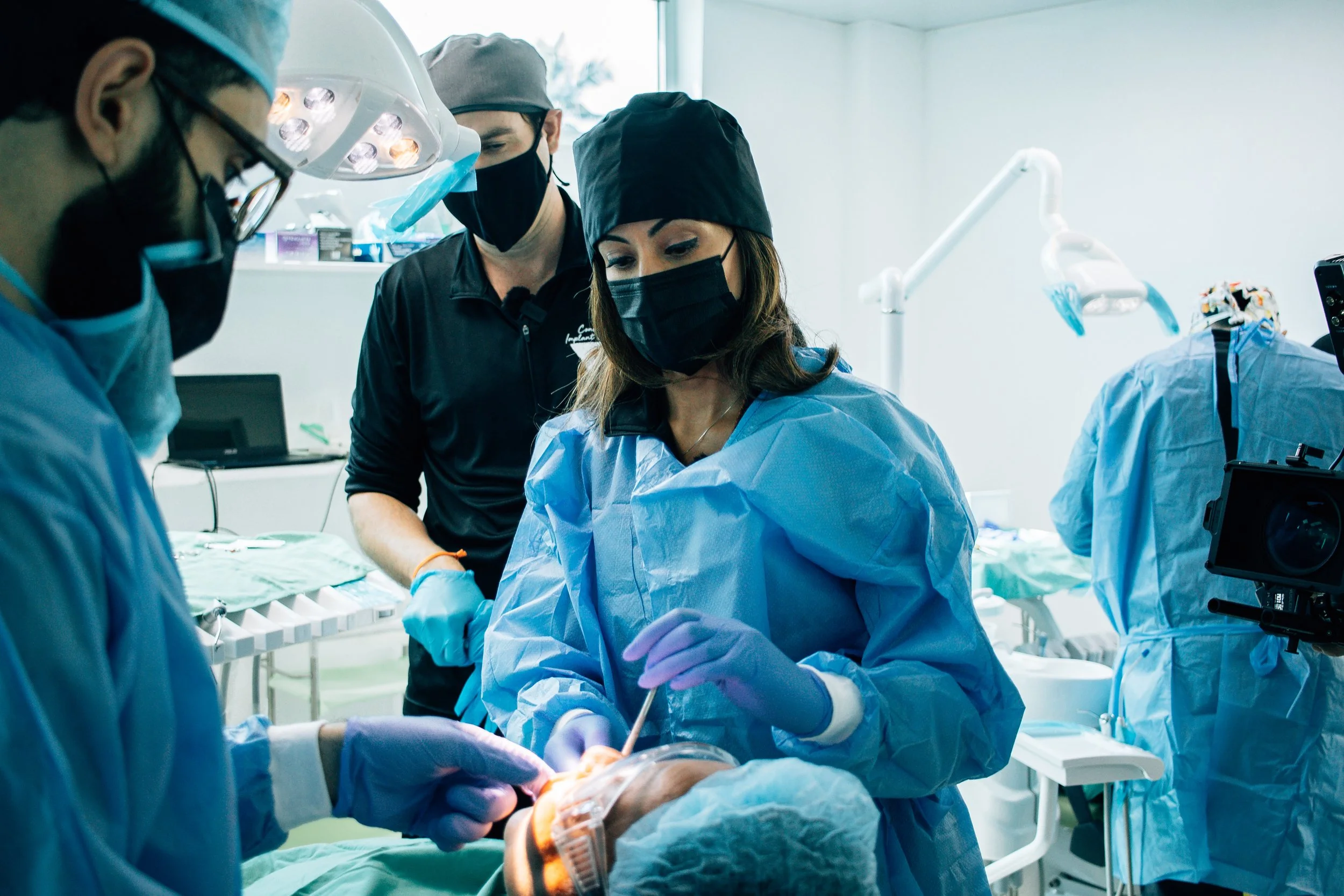 Medical team performing surgery in an operating room, with surgeons wearing scrubs, masks, and gloves, focused on a patient.