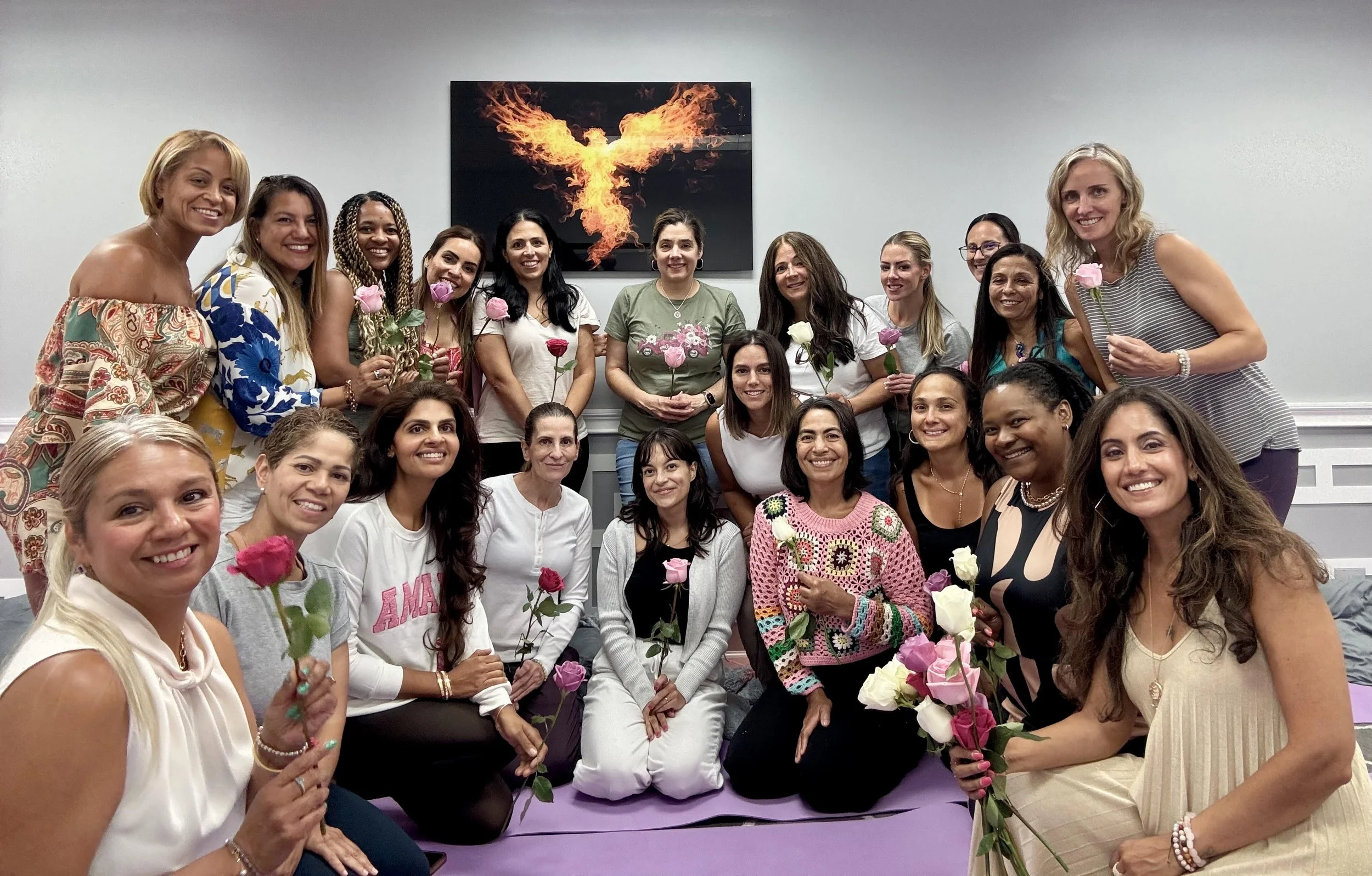 A group of women gathered in a room, some holding pink and white roses, smiling at the camera.