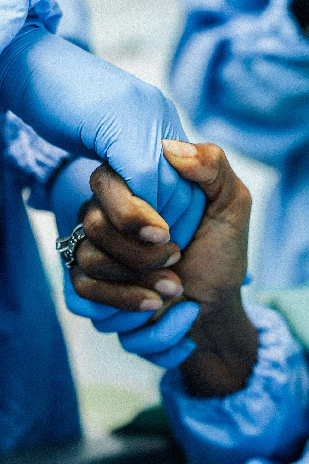 A healthcare worker wearing blue gloves holding a patient's hand.