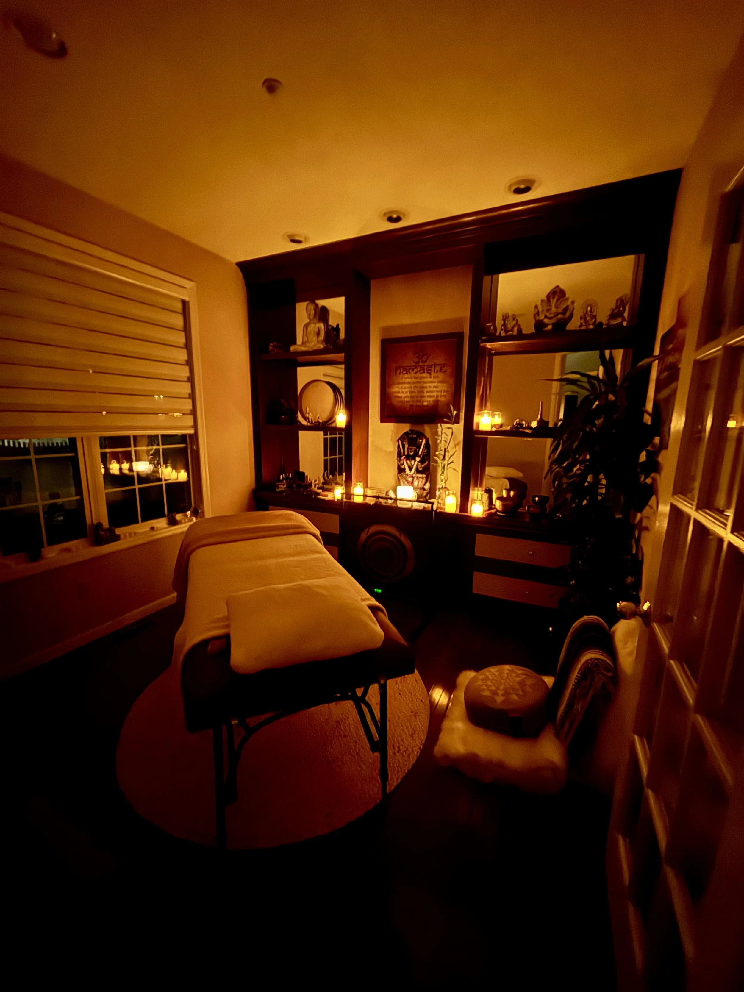 A dimly lit room with a massage table, ambient candles, and spiritual decor, creating a serene atmosphere.