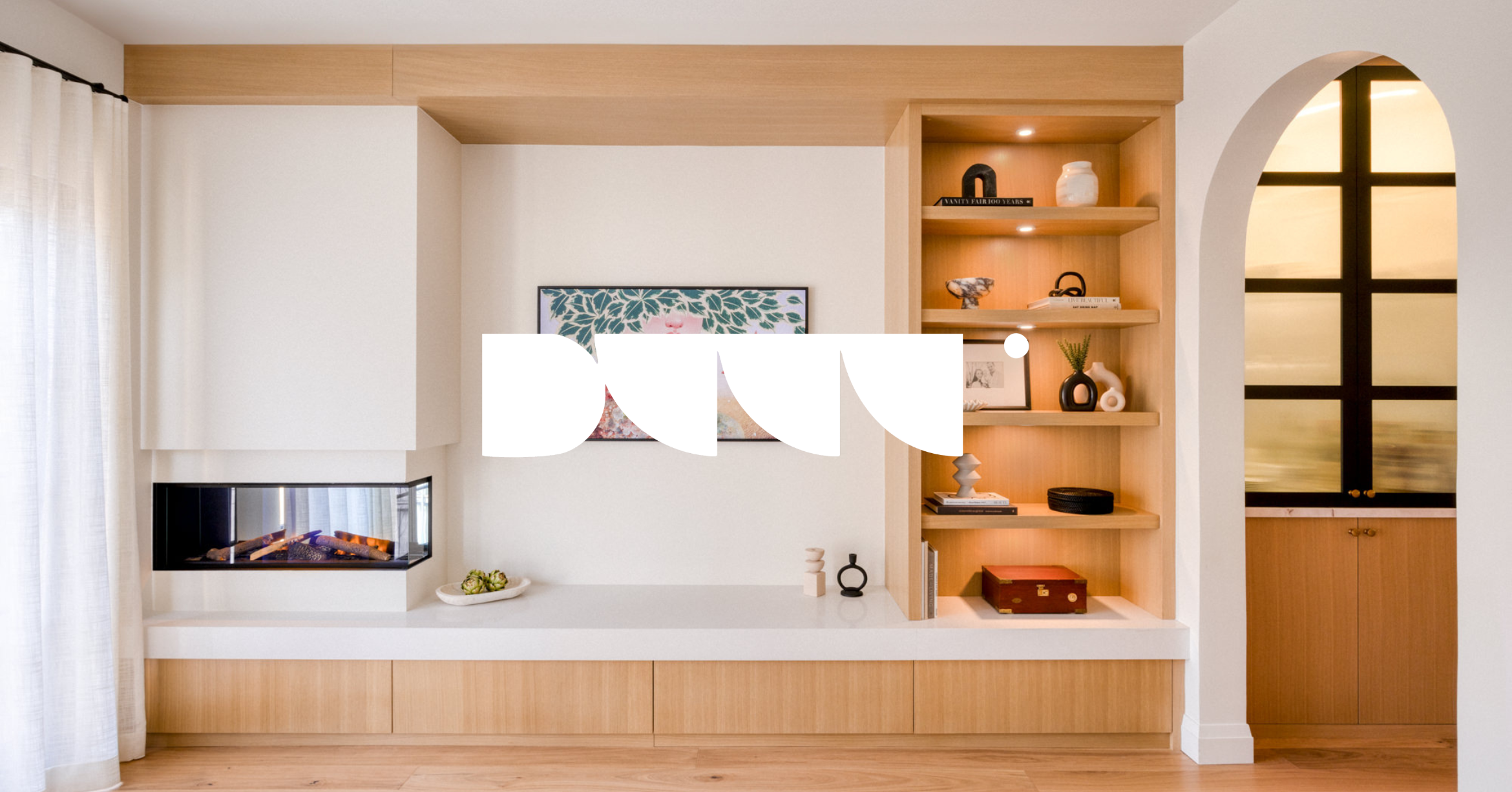 Modern living room with built-in white and wood shelving, a wall-mounted fireplace, artwork, decorative objects, and a large window with curtains.