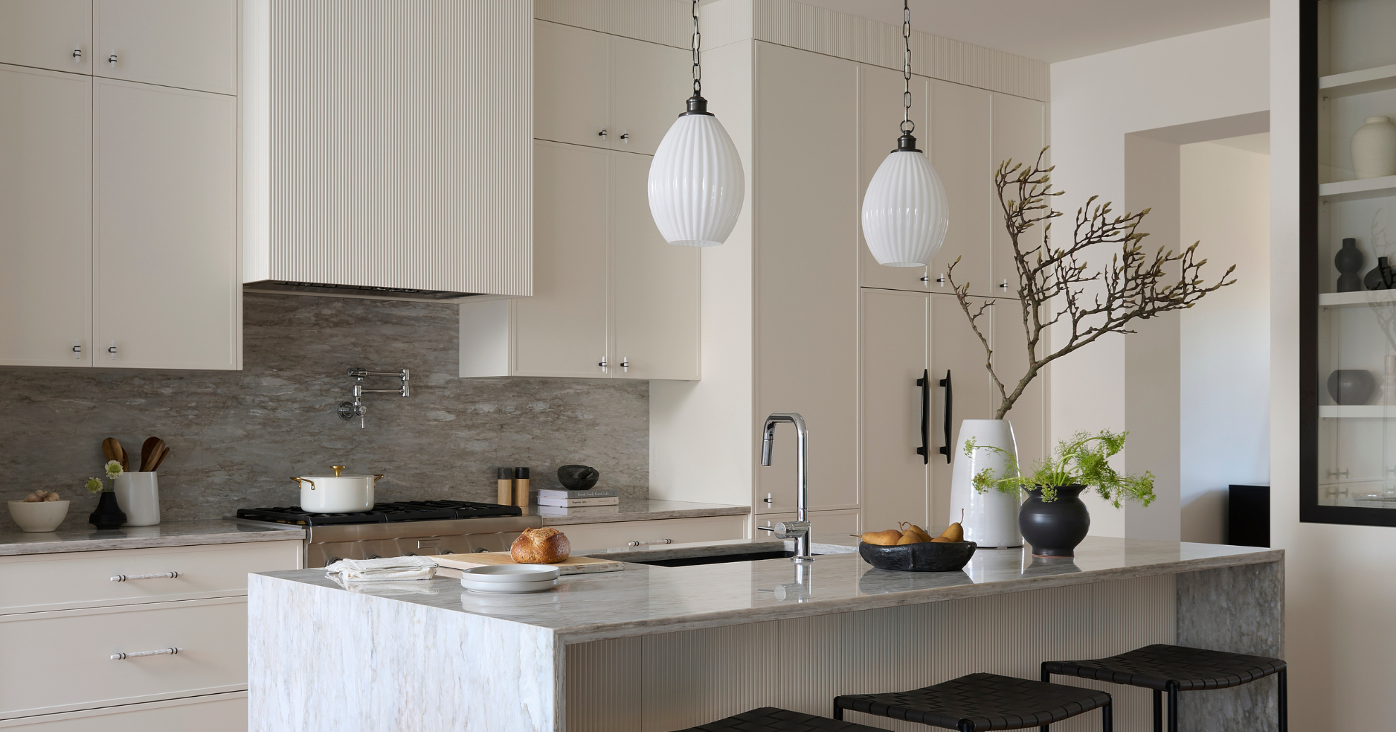Modern kitchen with cream cabinets, marble countertops, and a kitchen island decorated with vases and greenery.