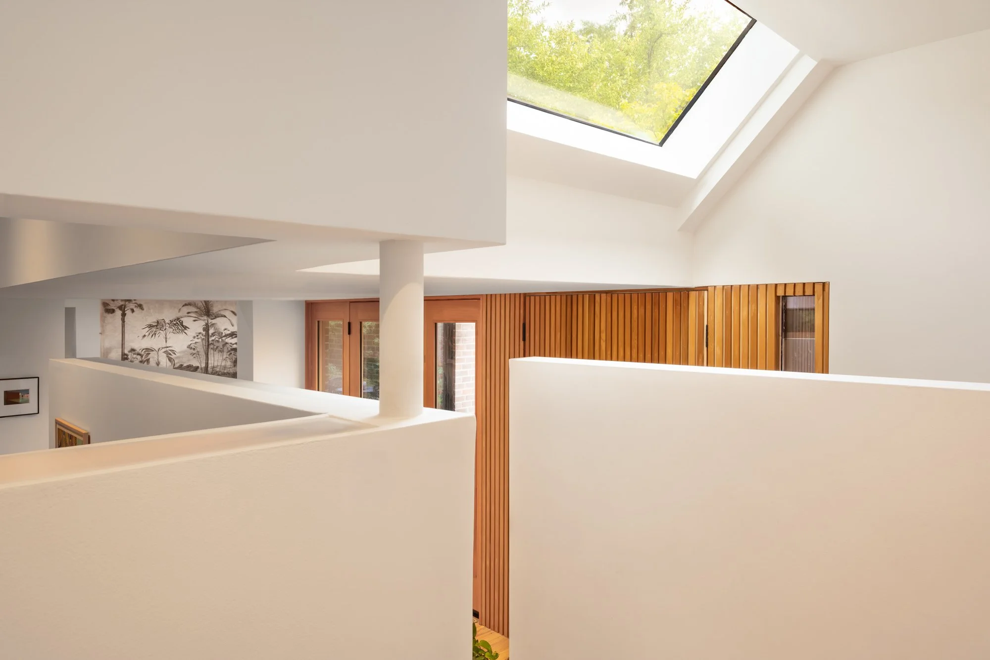 Interior view of a modern, minimalist home with white walls, a sloped ceiling, a skylight, and wooden sliding doors.