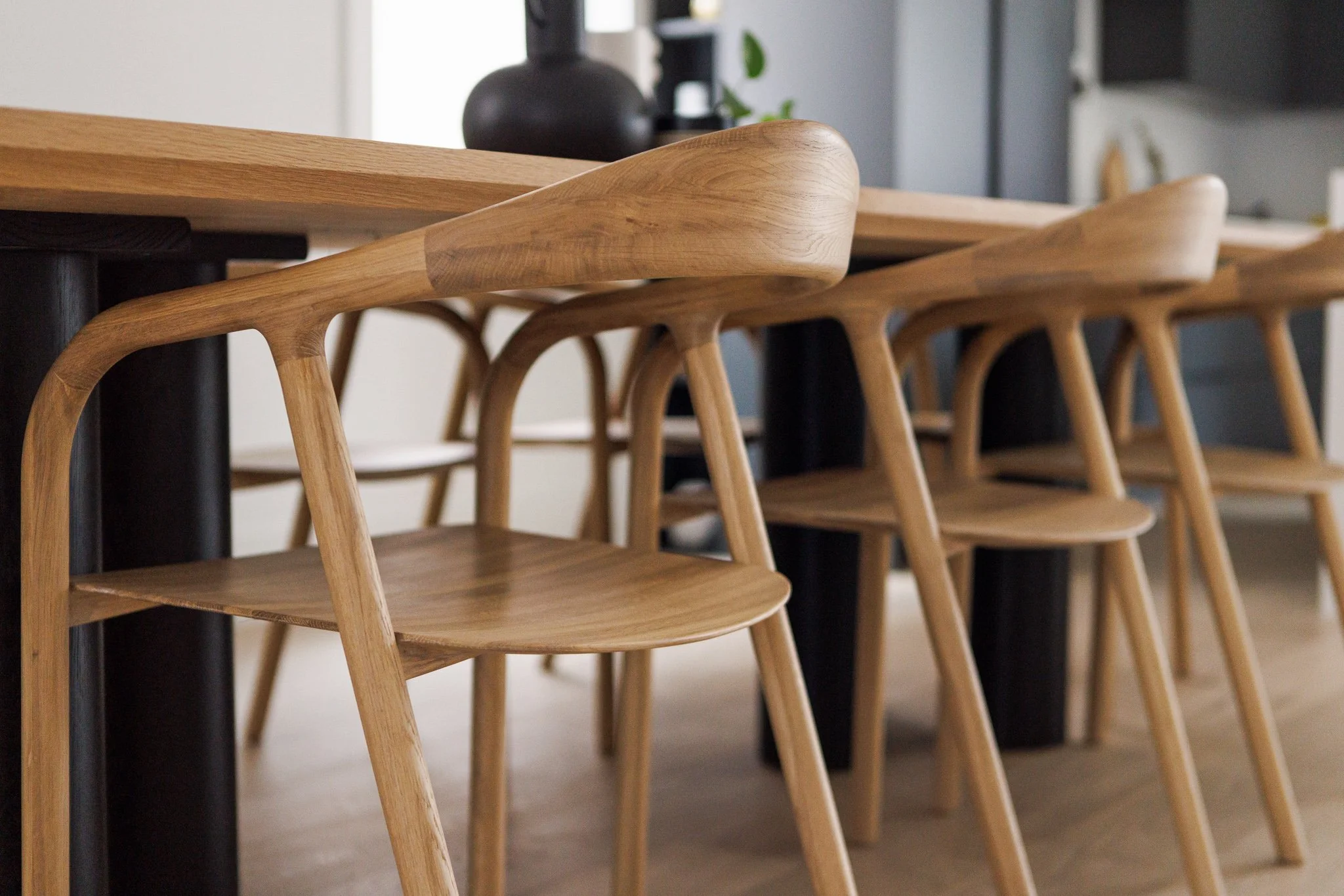 A row of wooden chairs with curved backrests lined up along a wooden table in a modern dining area.