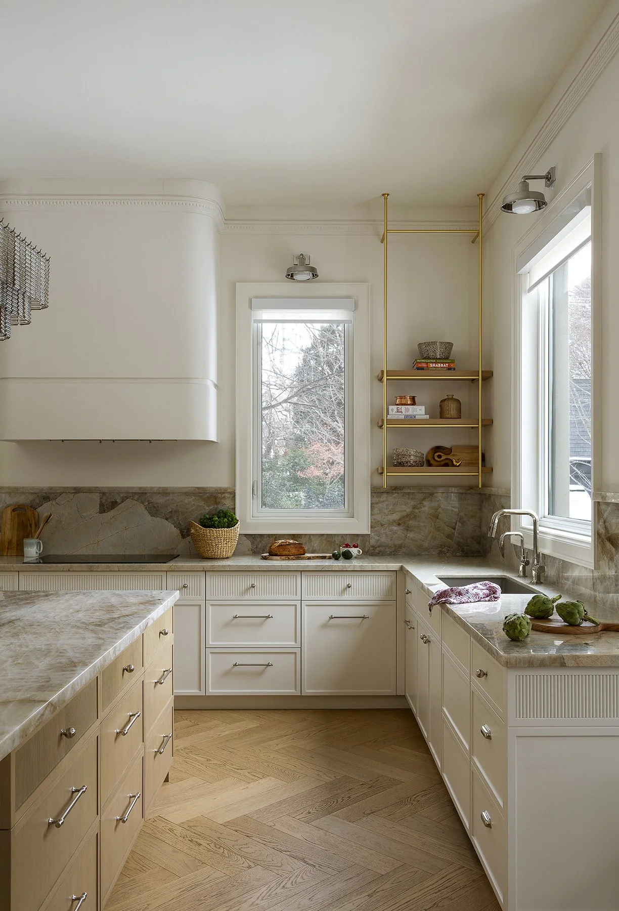 Modern kitchen with white cabinetry, marble countertops, wooden flooring, and large windows showcasing a view of trees.