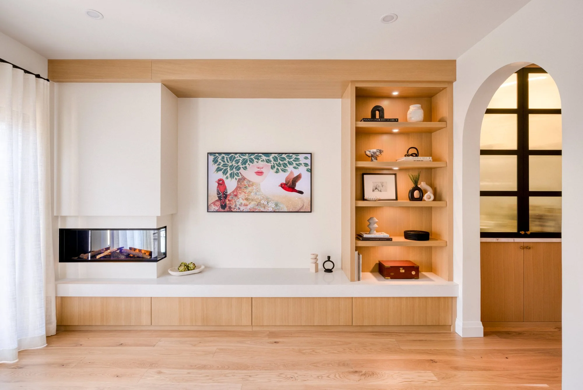 Modern living room wall with built-in shelves, abstract art, and a fireplace, featuring natural wood accents and minimalist decor.