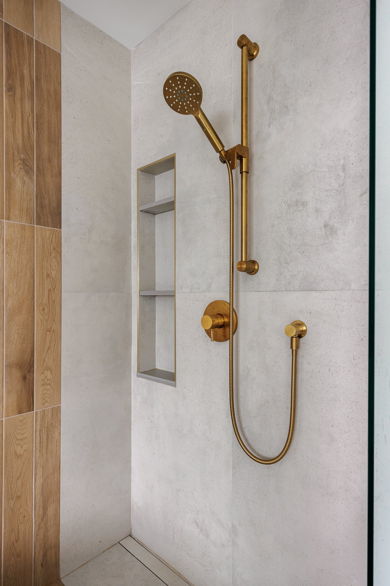 Brass showerhead and fixtures in a modern shower with beige and wood-tiled walls.