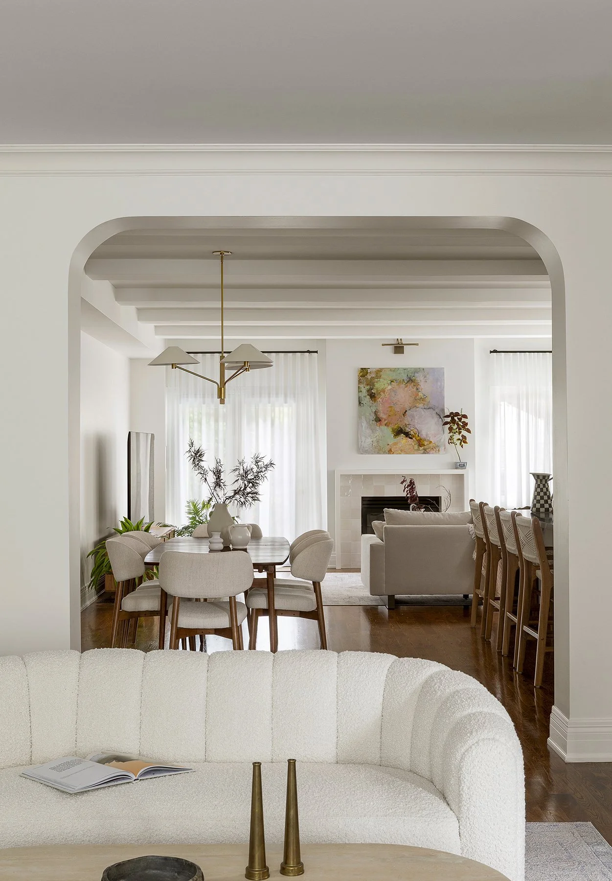 Living and dining room with white and beige furniture, wooden flooring, art on the wall, plants, and a fireplace.
