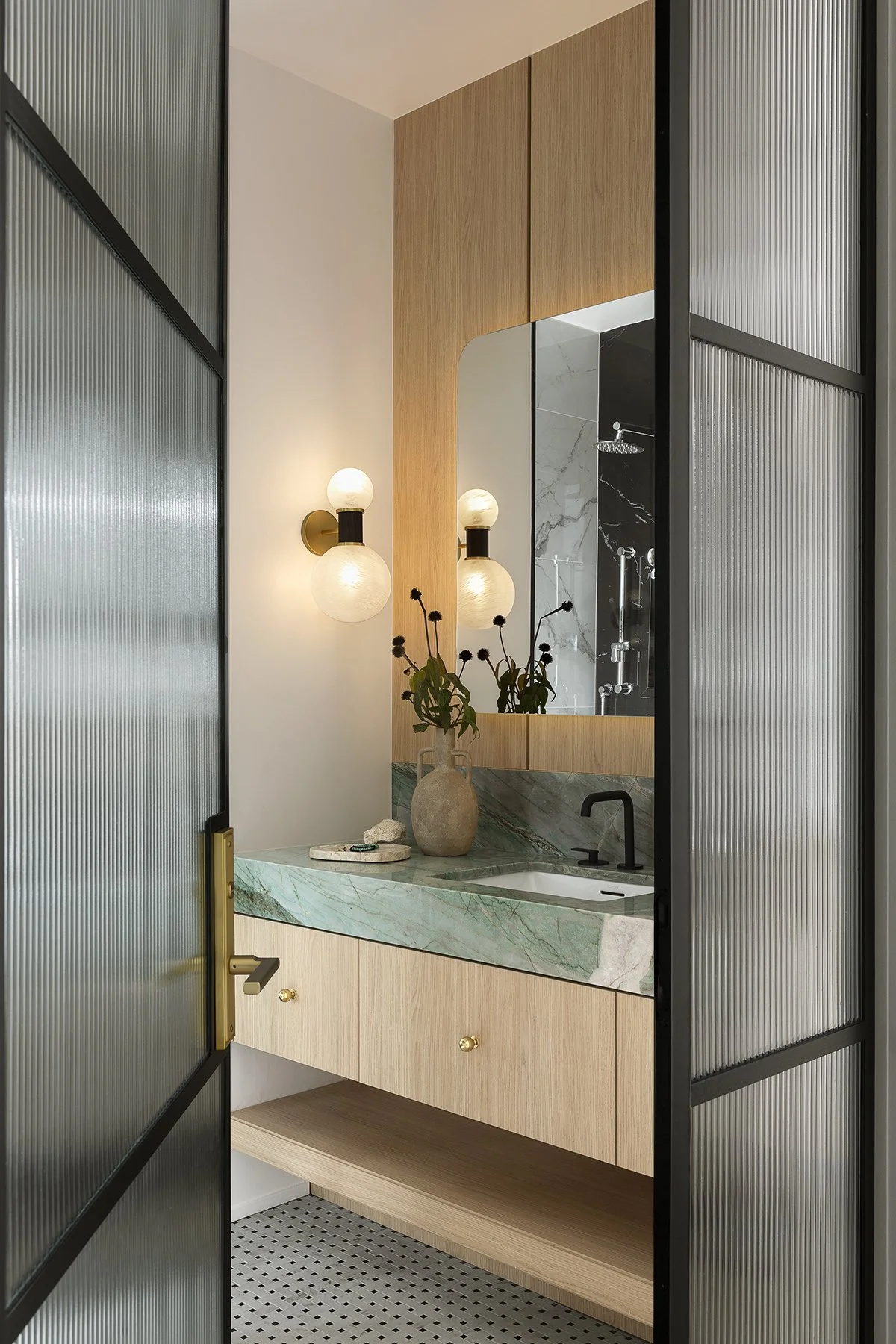 Modern bathroom with a green marble sink, wooden cabinets, and textured glass doors.