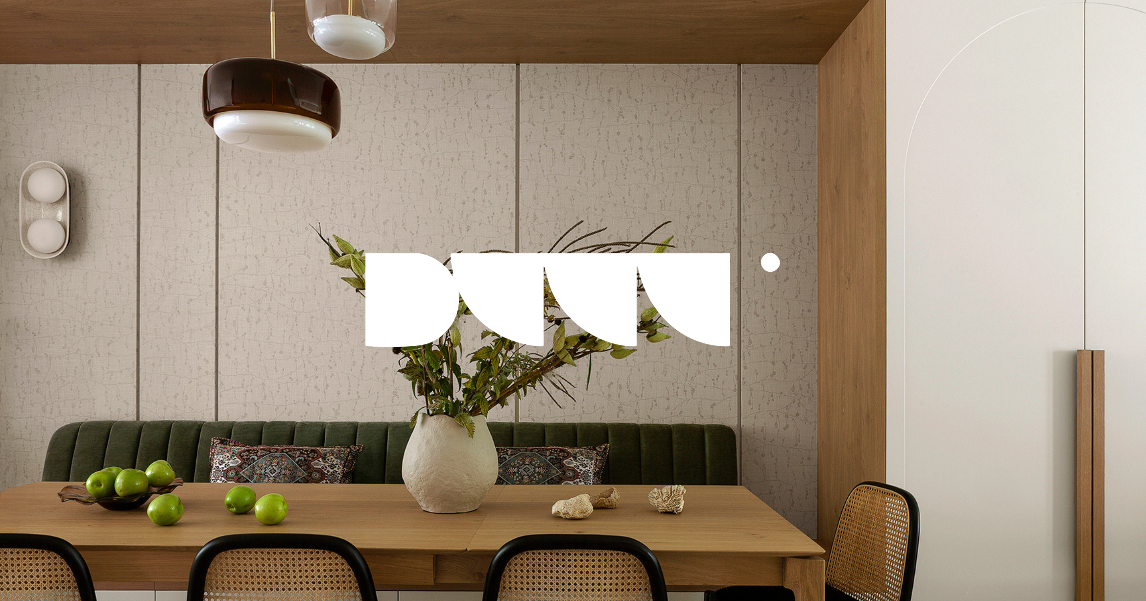 Modern dining room with a wooden table, a vase with greenery, green apples, decorative shells, a bench with patterned pillows, hanging pendant lights, beige textured wall panels, and a white cabinet.