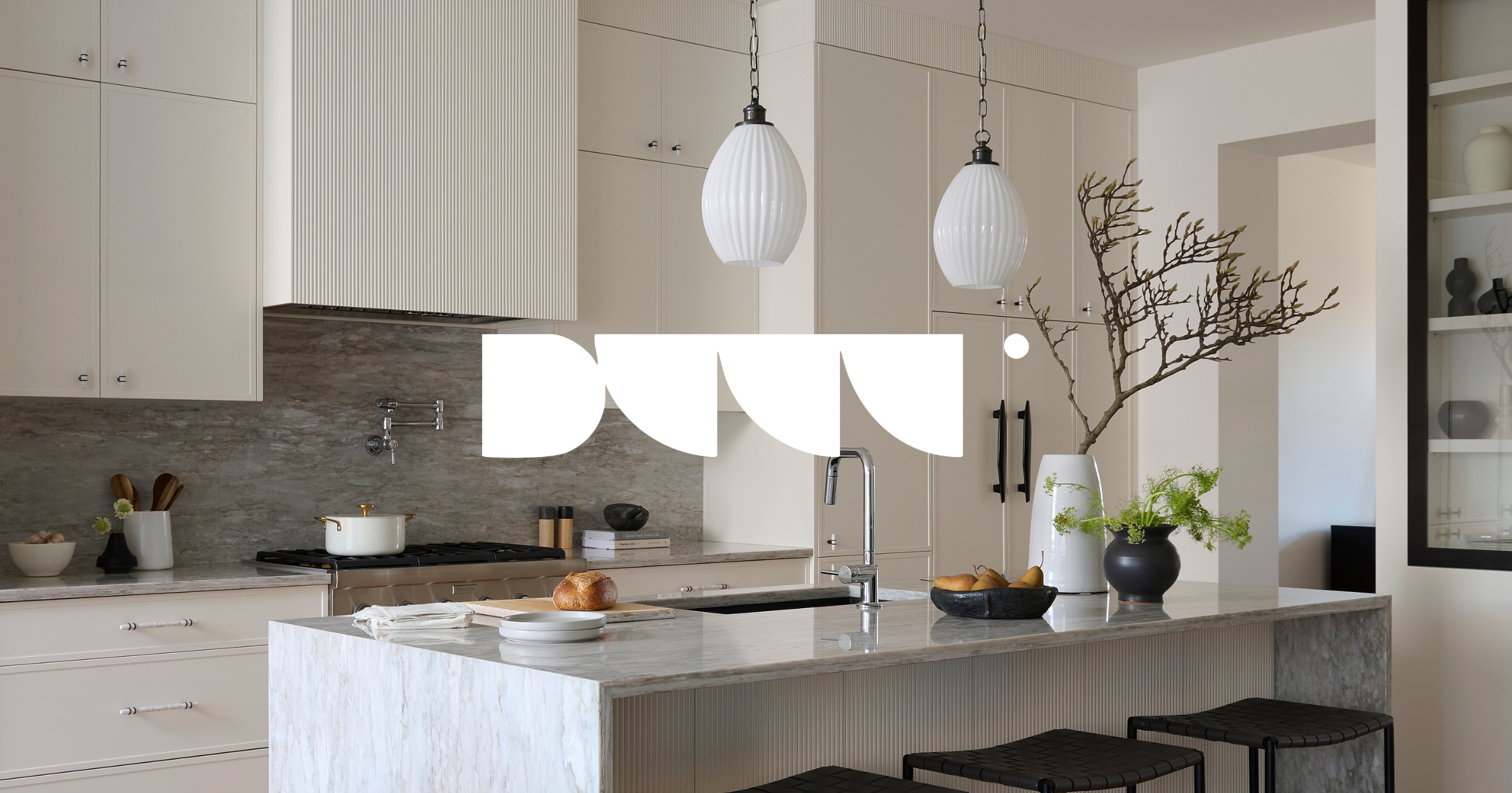 Modern kitchen with white cabinets, a marble island, two hanging pendant lights, and decorative vases with plants and branches.