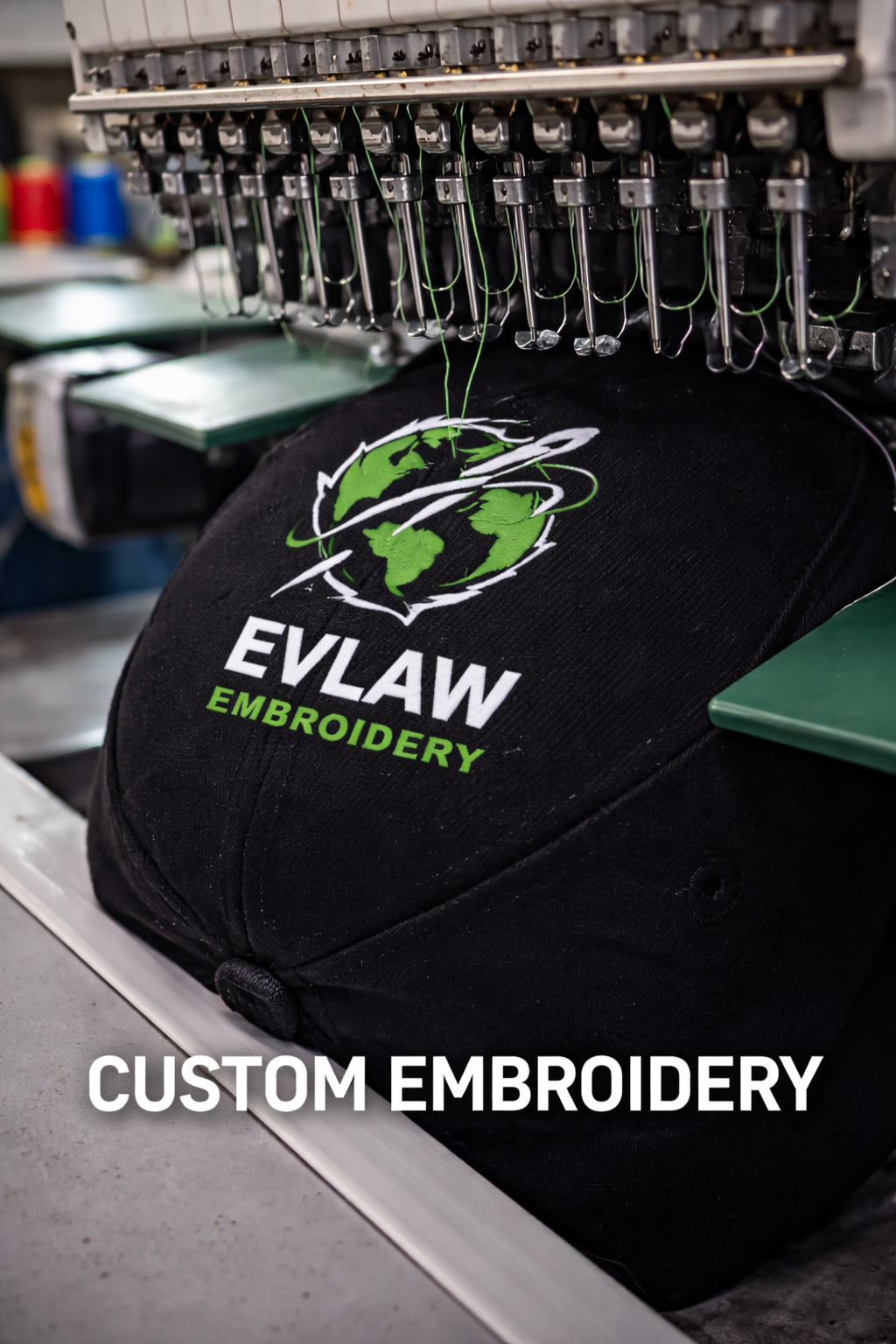 Close-up of an embroidery machine stitching a logo on a black fabric bag. The logo features a globe with green continents and white rings, with the text 'EVOID WR' and 'EMBROIDERY'.