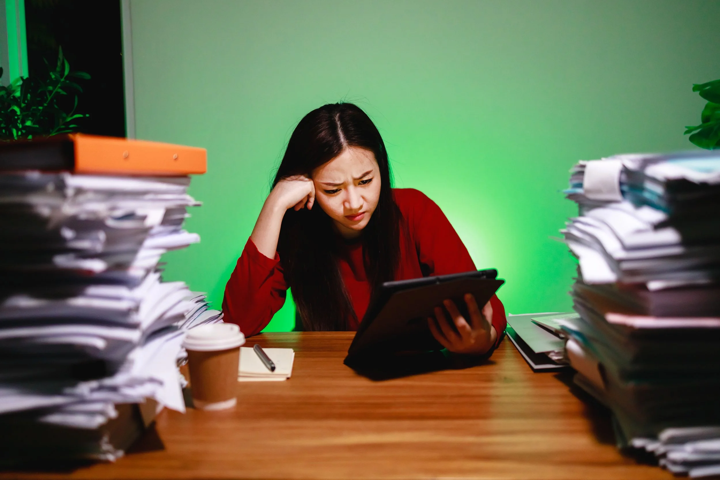 Stressed out woman looking at her tablet surrounded by piles of paper