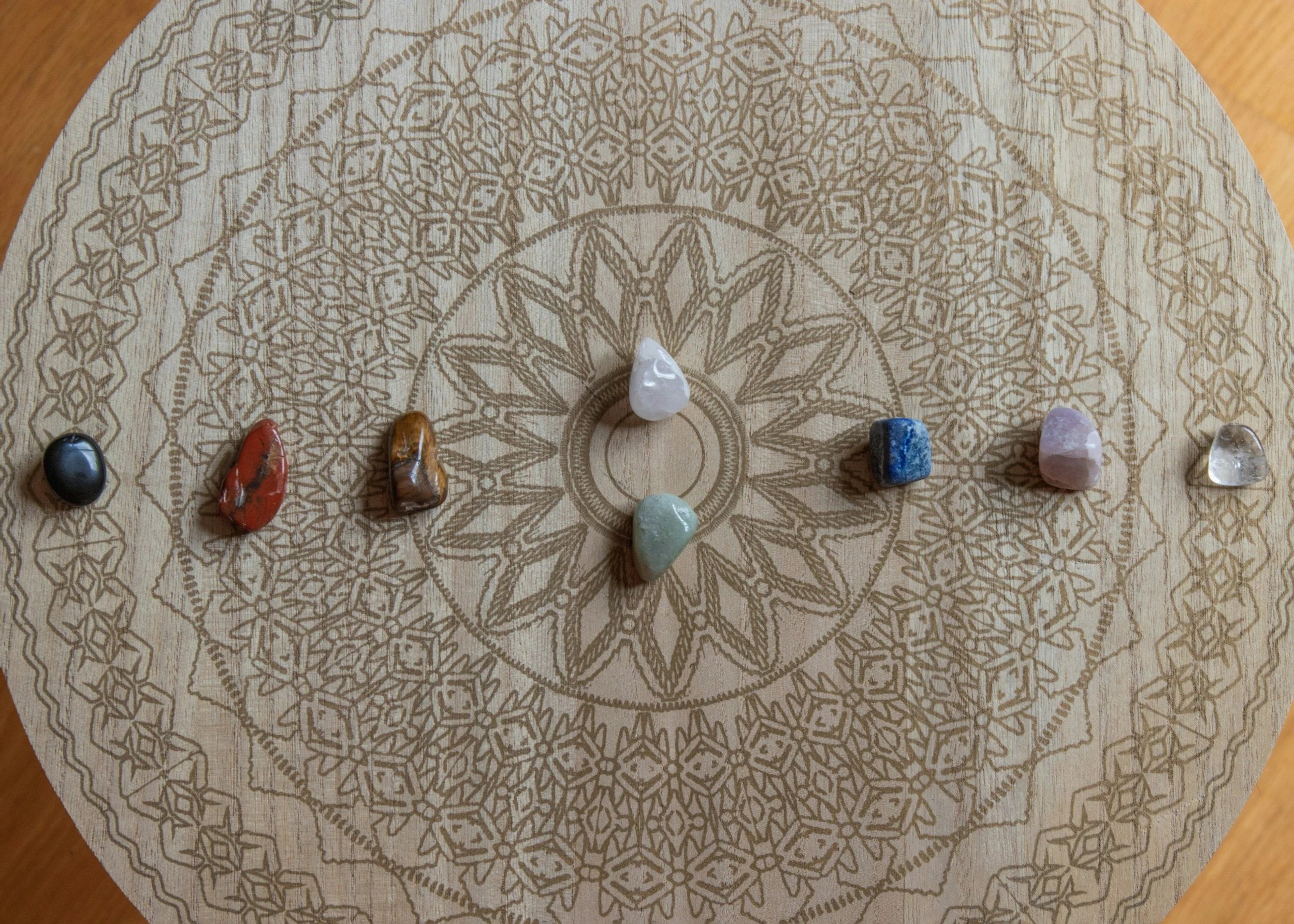 A wooden circular board with intricate geometric patterns engraved on it, with eight different polished gemstones arranged in a circle on the board.