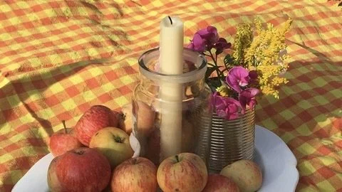 Apples arranged around a candle and flowers on an orange-and-yellow checked cloth for a Lammas celebration.