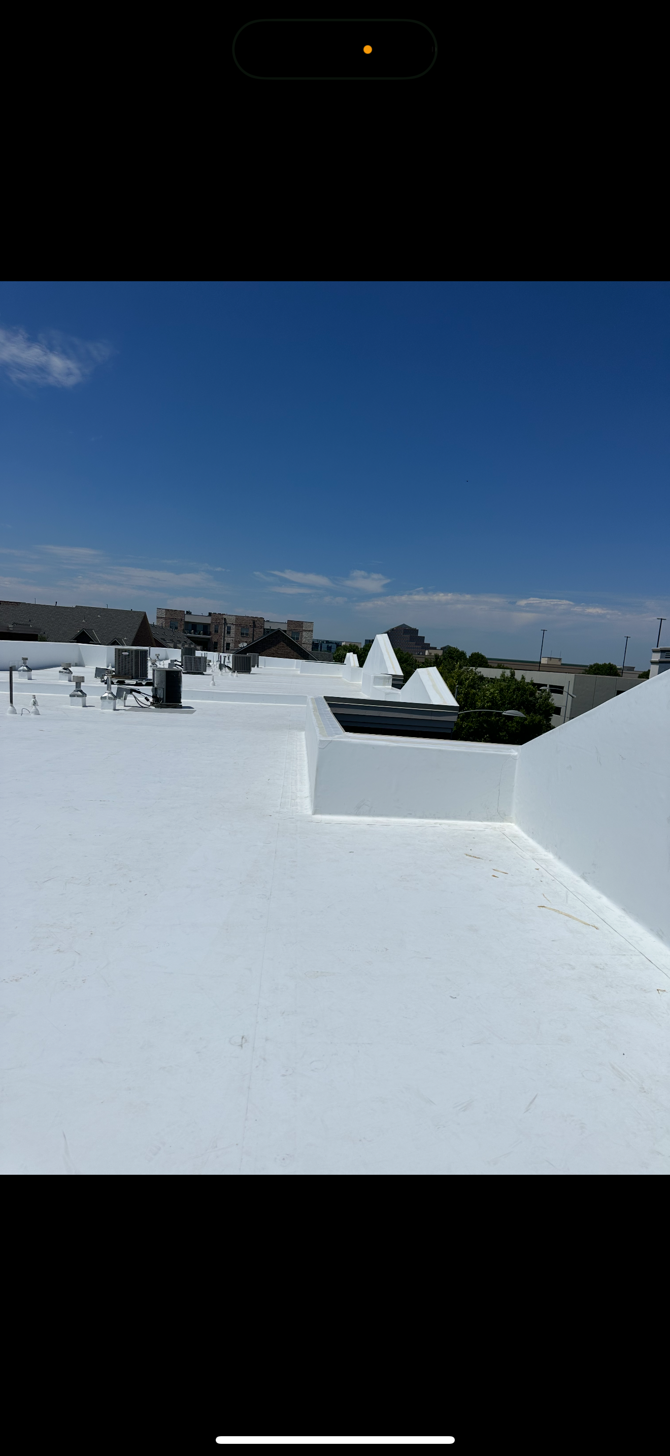 Flat white rooftop with vents and HVAC units under a bright blue sky with some clouds.