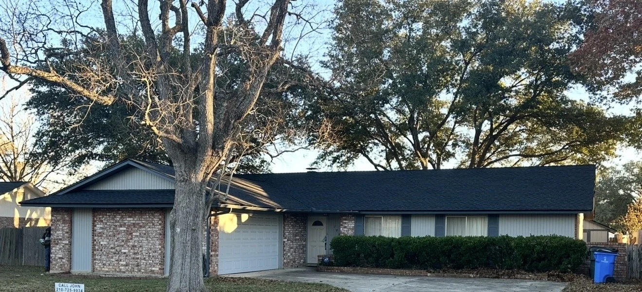 Single-story house with brick and siding exterior, large front yard with a tree, bushes near the front door, driveway, and a trash bin.
