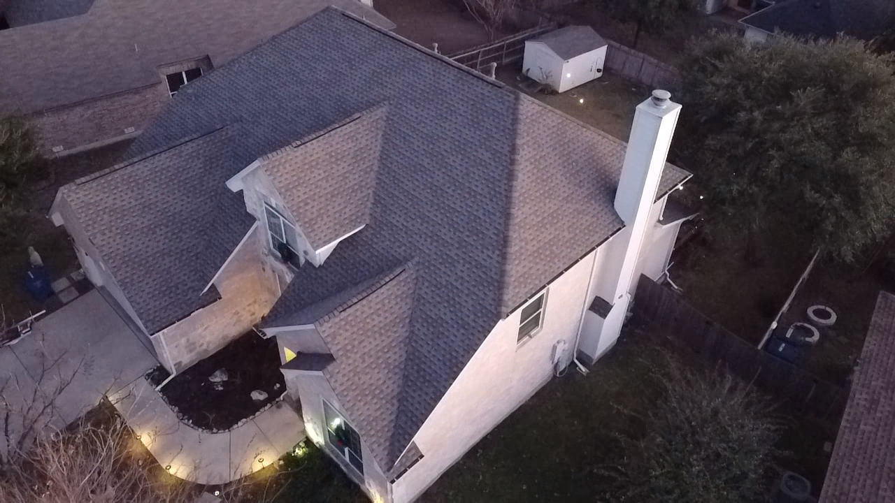 An aerial view of a two-story house with a multi-sectioned roof, chimney, and backyard at dusk.