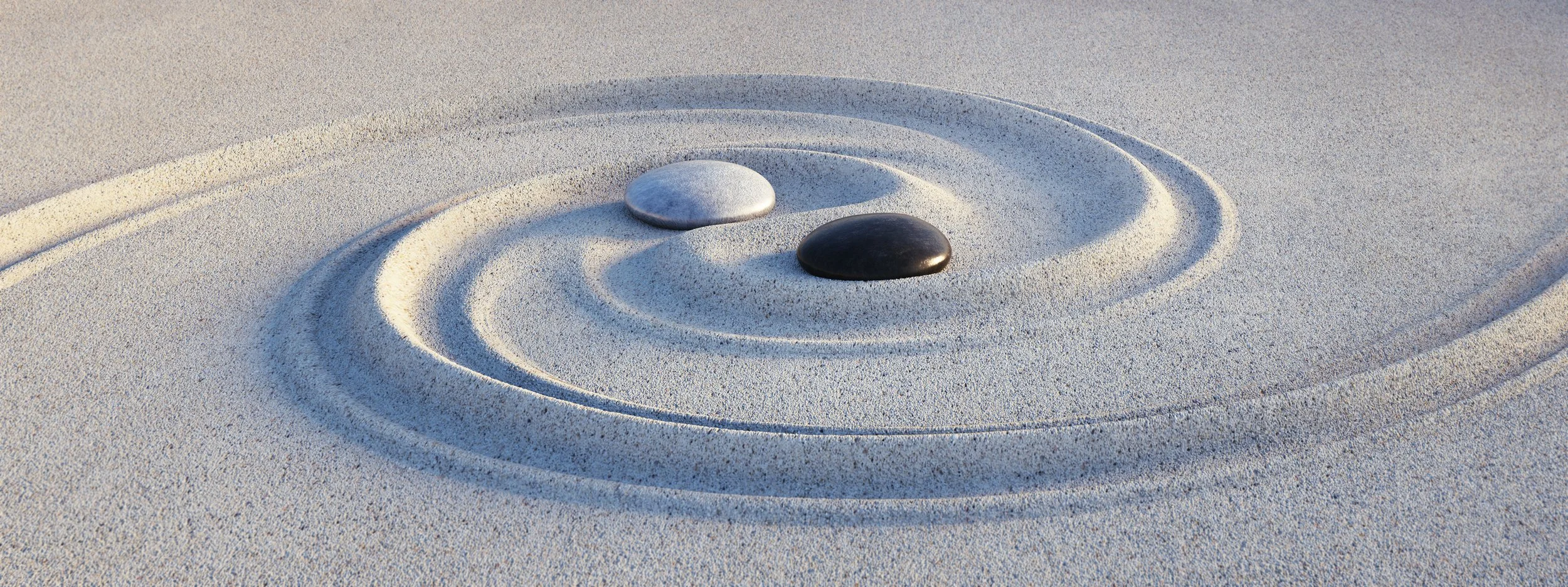 Close-up of two stones, one white and one black, placed on white sand creating concentric circles around them.