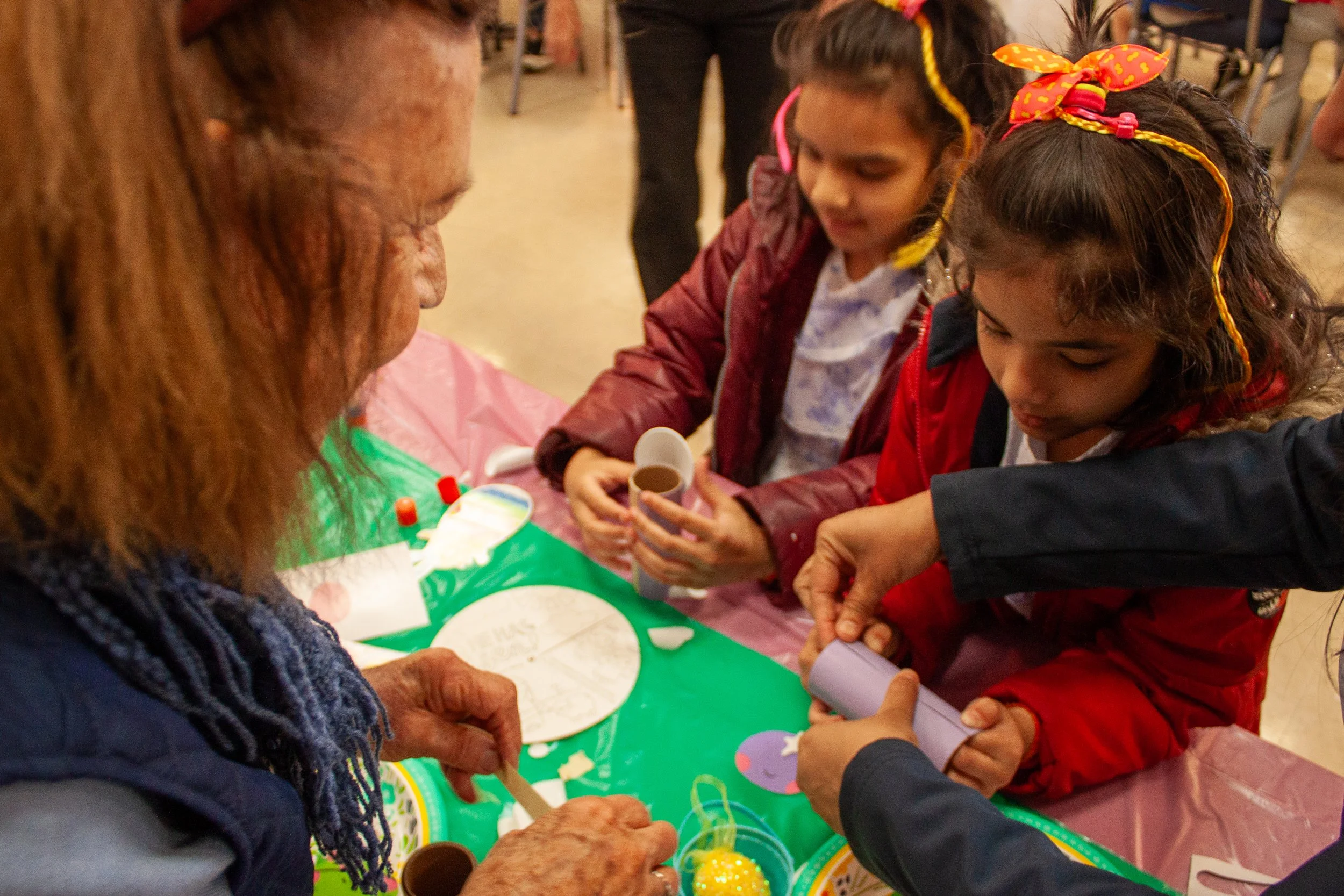 Children and adults gathered around a table decorating Easter eggs with paint and stickers.