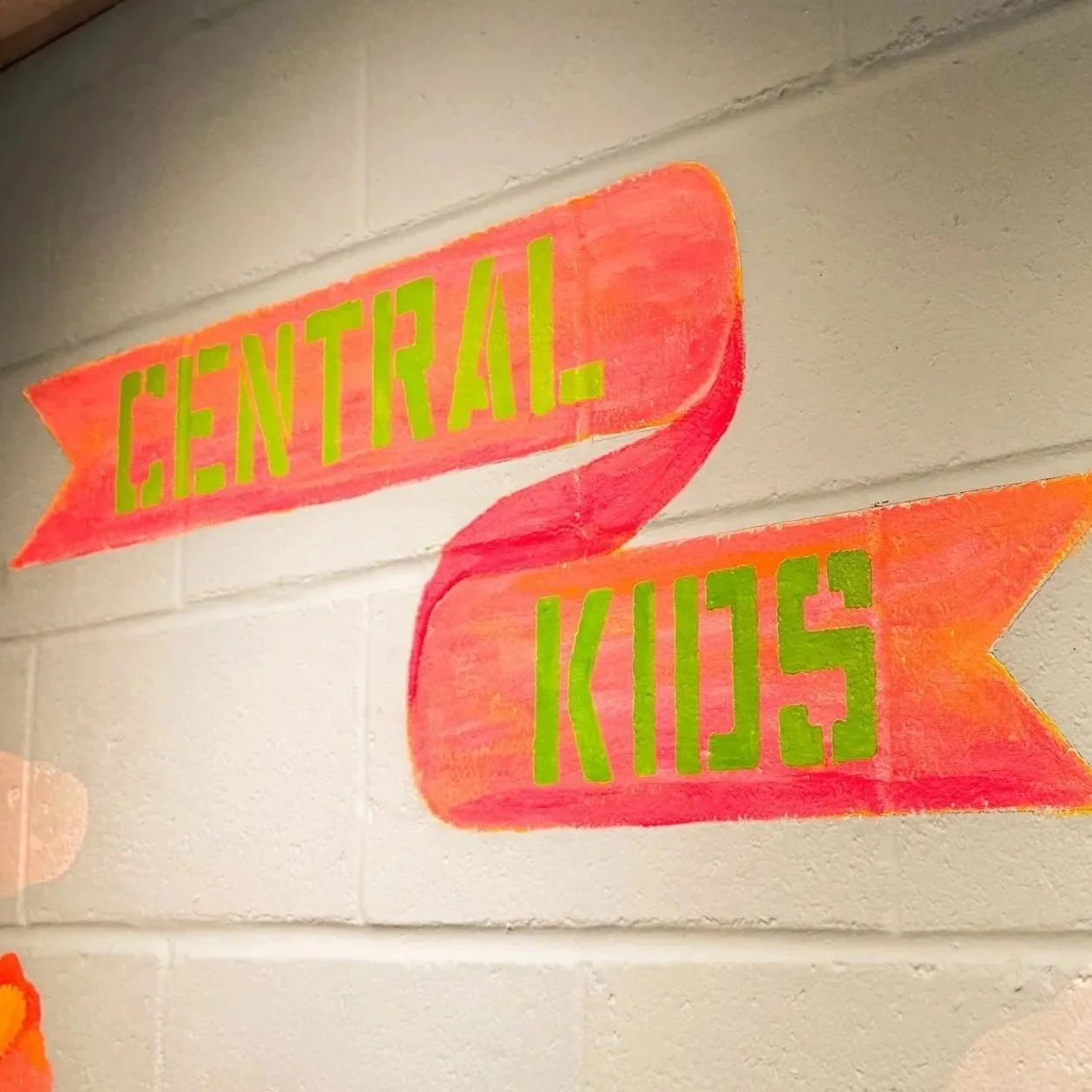 Colorful hand-painted sign on a brick wall with the words 'Central Kids' written in green inside orange banners.