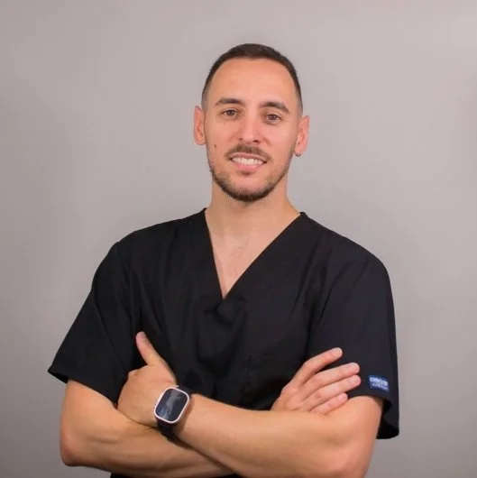 Hombre con uniforme oscuro y pulsera inteligente, sonriendo con brazos cruzados