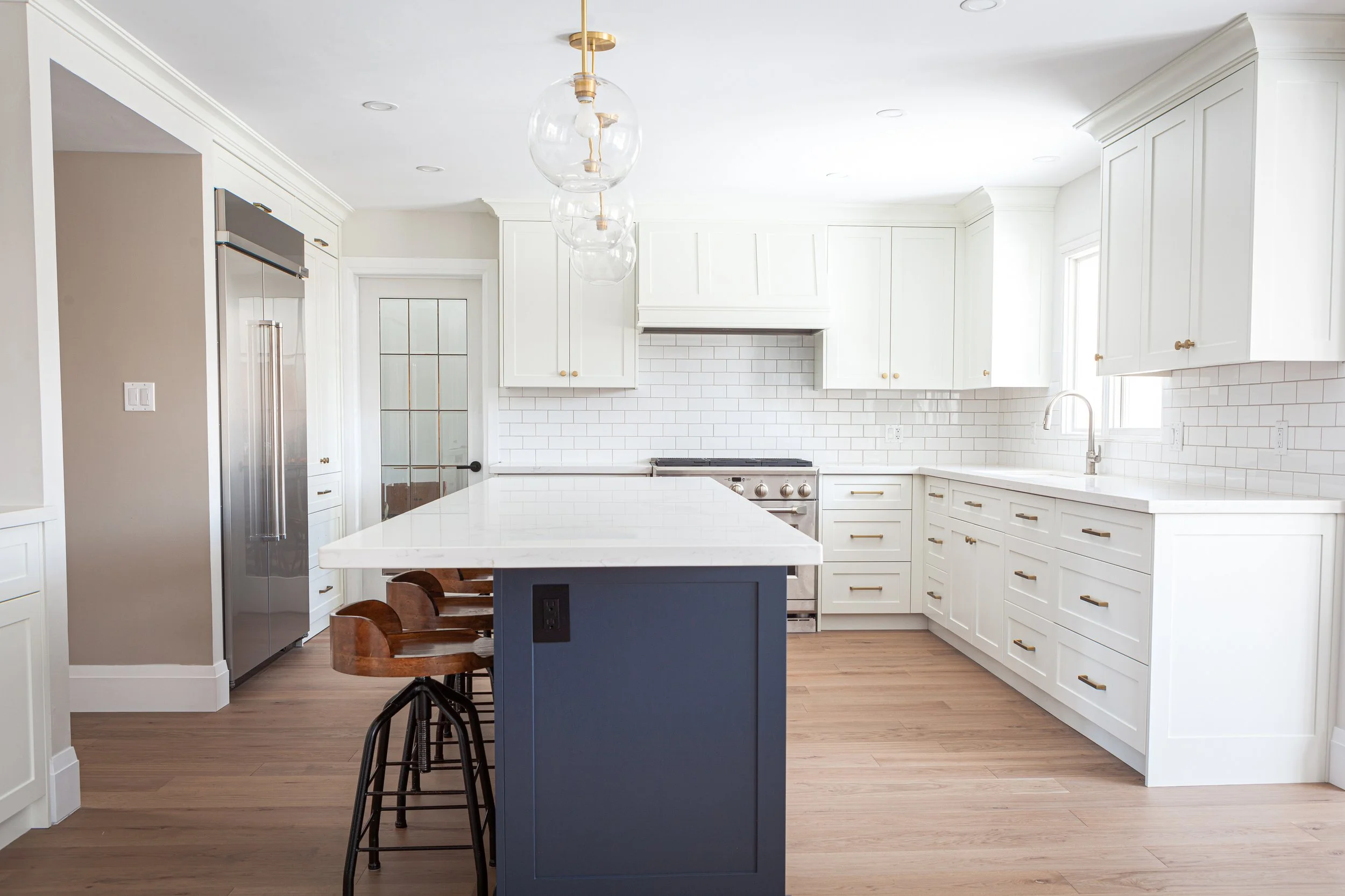 A beautiful kitchen feature white cabinetry, a dark blue island, and gold accents on the hardware and light fixtures shows the potential of Kitchener Waterloo Contractors Berlin Contracting.