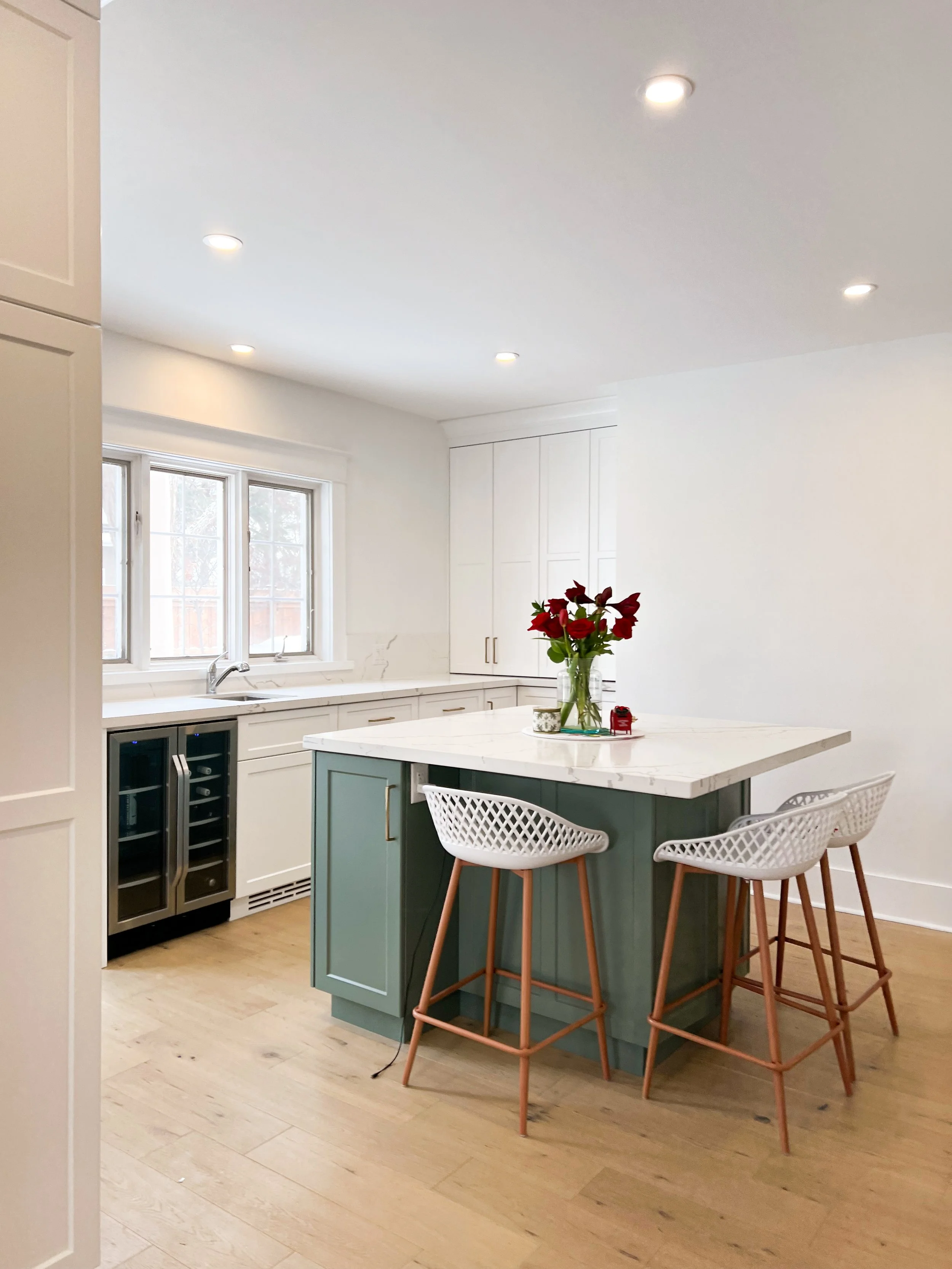 A bright kitchen filled with natural light, featuring the work of General Contractor in Kitchener. The exterior finishes are white, with a beautiful green island surrounded by basket weave stools.