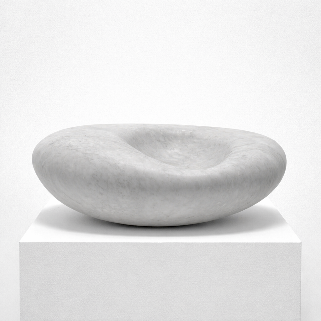 Carved from solid marble, this minimalist form balances weight and softness, its rounded exterior gently folding inward to create a quiet central hollow. Carrara marble