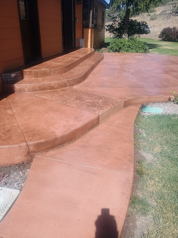 Red concrete steps leading to a door, with a curved walkway in front, next to a green lawn and garden area.