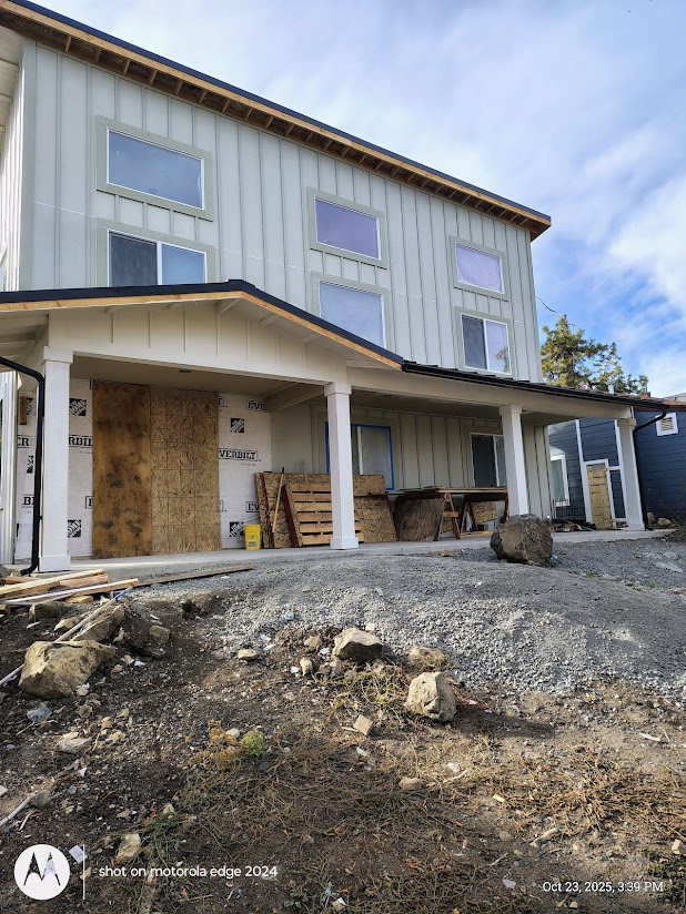 Back of a house under construction with a partially finished deck, construction materials, and rocks on the ground.