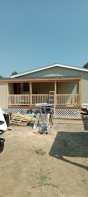 Front view of a house with a partially built wooden porch, construction tools, and materials in the yard under a clear blue sky.