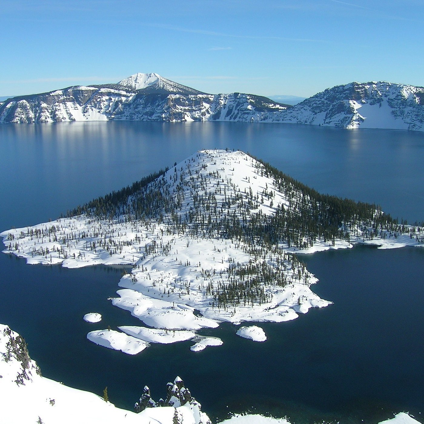 Snow-covered volcanic island in a lake with a mountain and cliffs in the background.