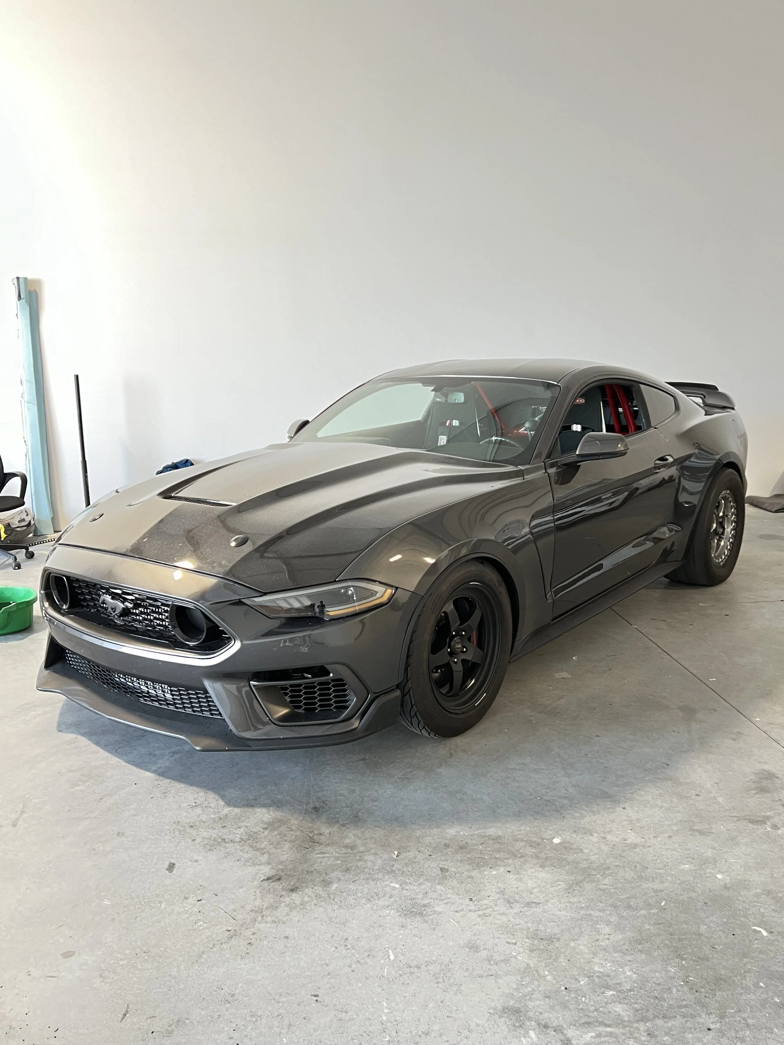 A black Ford Mustang sports car with custom wheels parked in a garage.