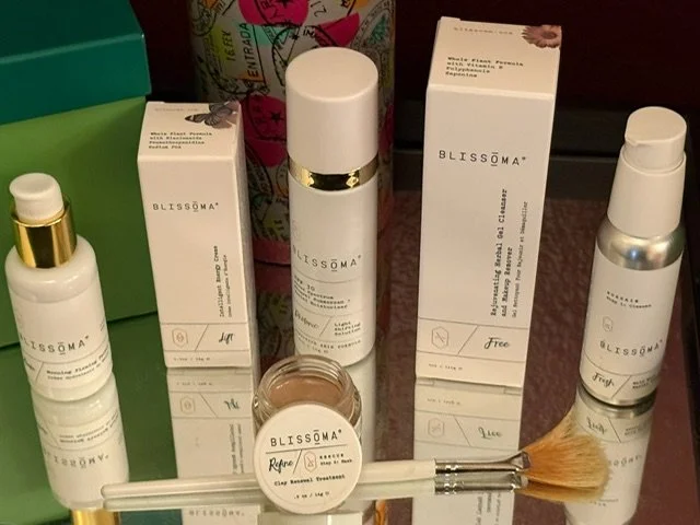 Collection of Blissöma skincare products including bottles, jars, and boxes displayed on a surface, along with a makeup brush.