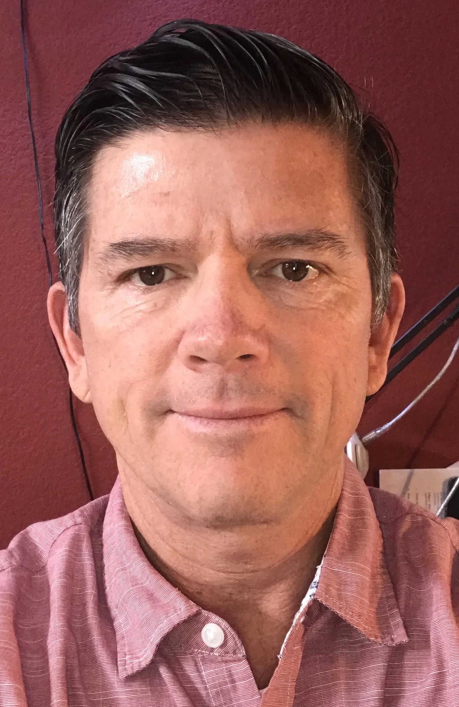Man in a pink button-up shirt against a red background.