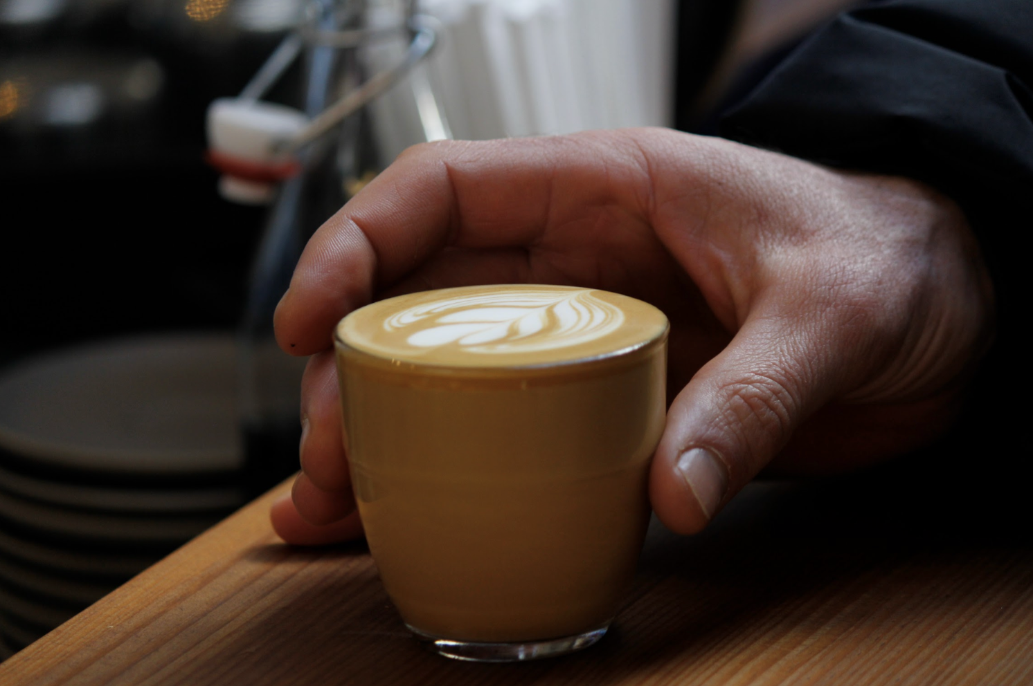 Close-up of a hand holding a glass of latte with latte art on wooden table.