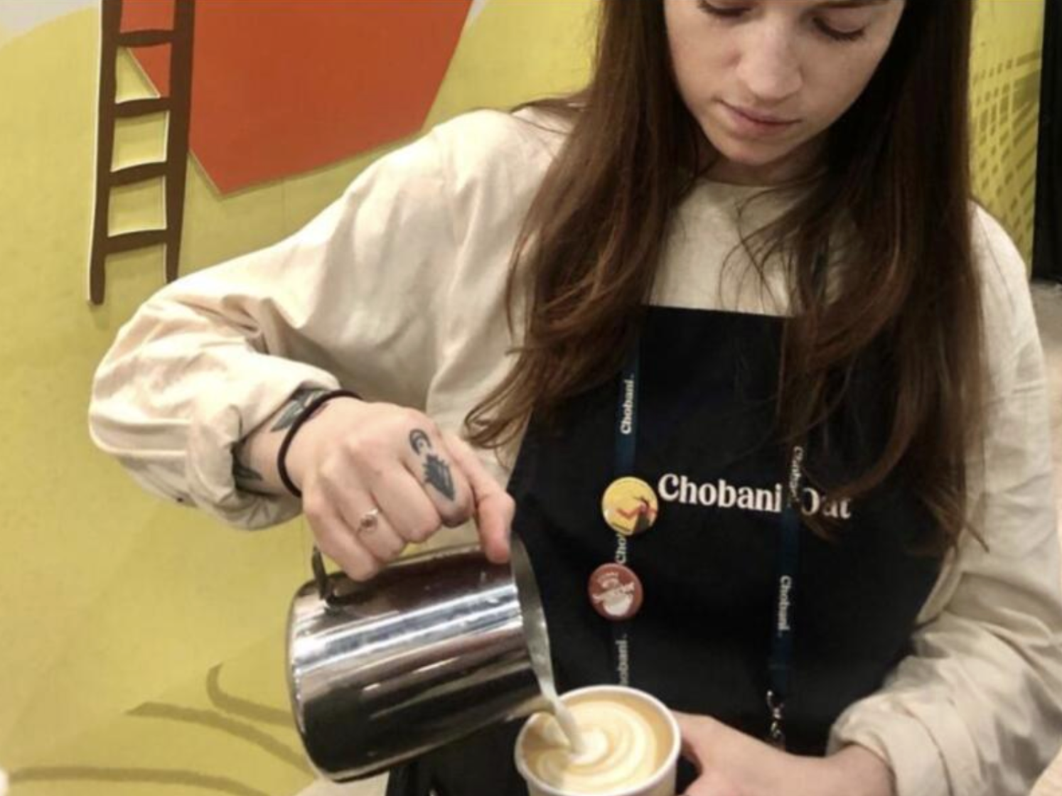 Barista pouring latte art into a cup at a promotional event for Chobani Oat.