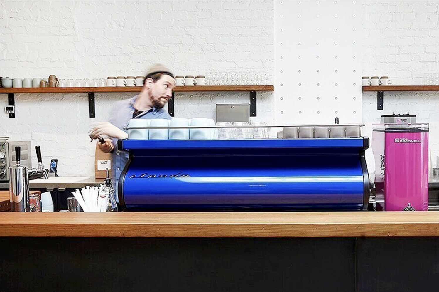 Barista behind a counter with a blue espresso machine and coffee cups.