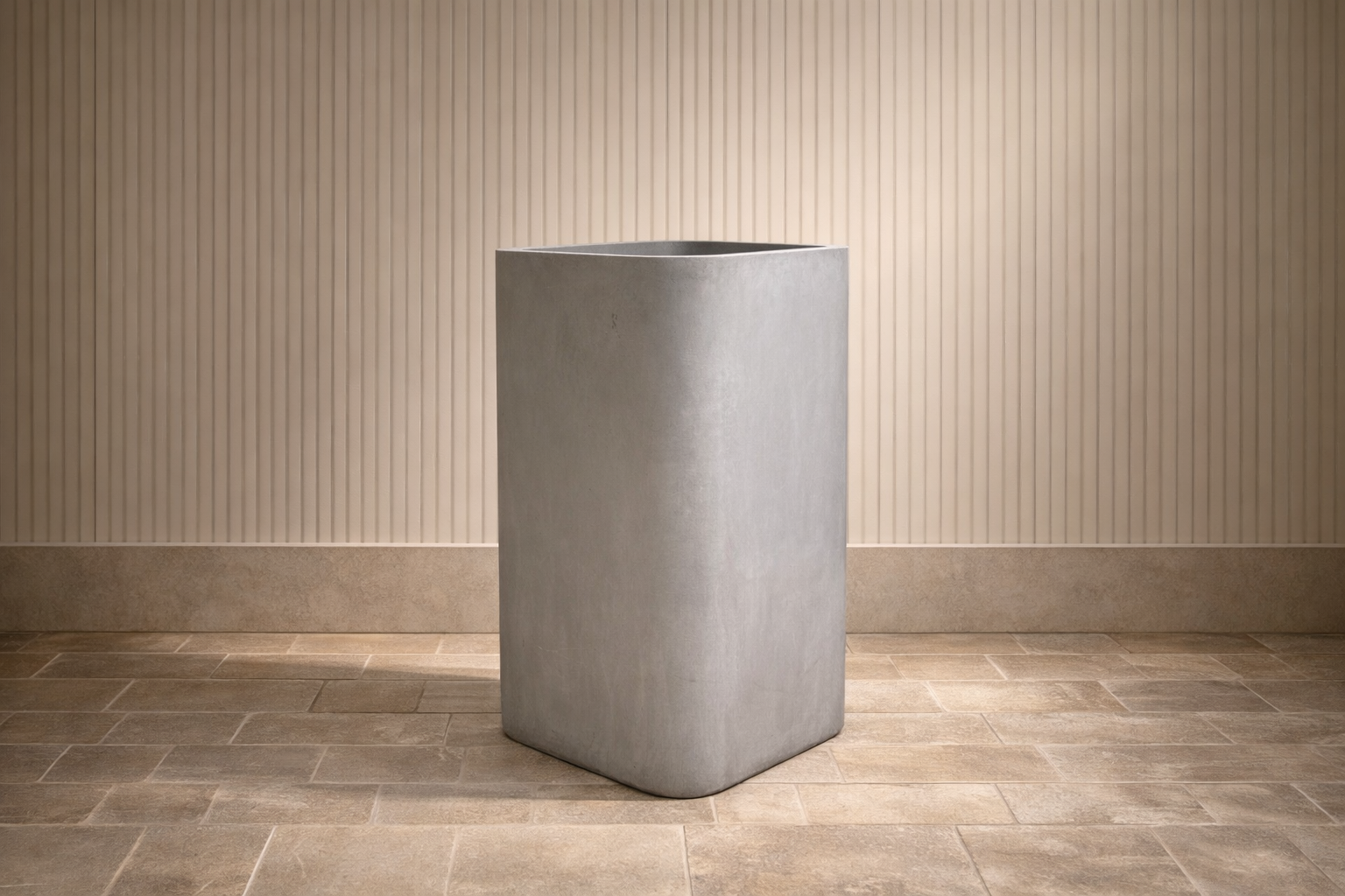 A tall, rectangular, gray concrete planter on a tiled floor in front of a vertically striped beige wall.