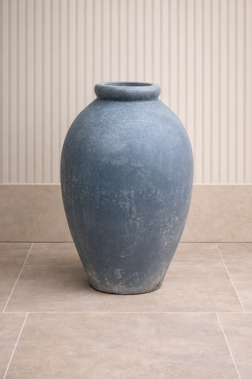 Large, blue ceramic vase with a crackled finish, placed on beige tile floor against a background of vertically striped wall paper.