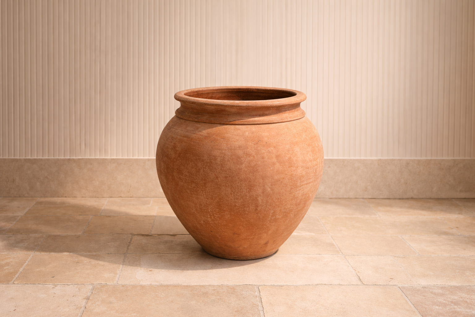 Large empty terracotta vase placed on beige tiled floor against a beige wall.