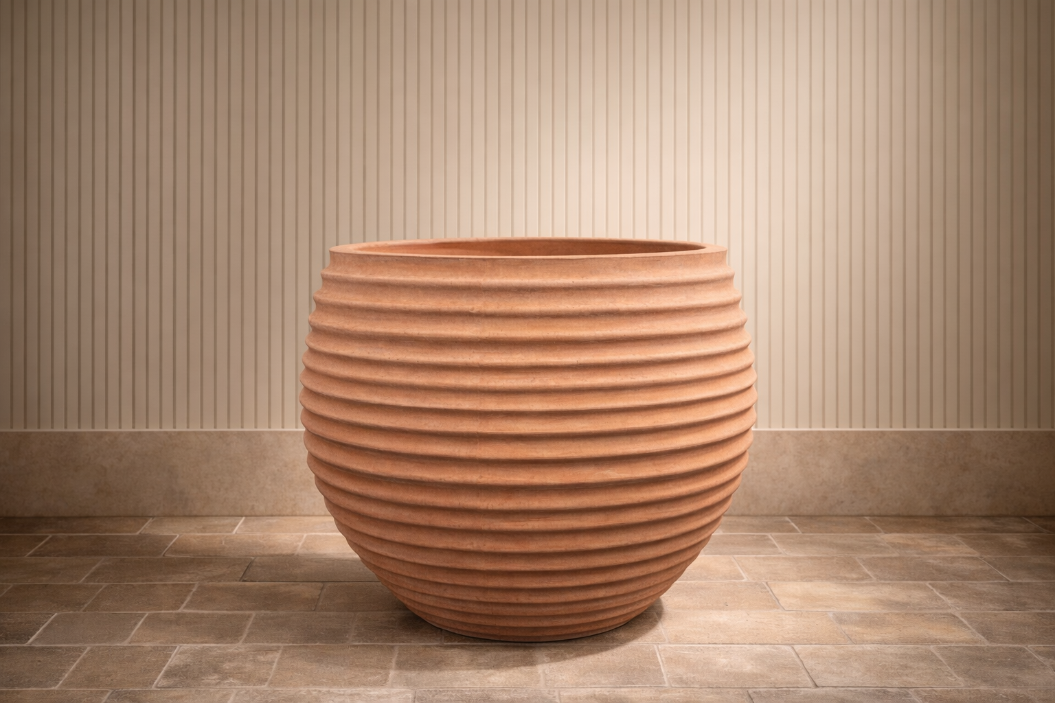 A large, ribbed, terracotta-colored ceramic planter with no plants inside, placed on a tiled floor in front of a beige wall with vertical stripe texture.