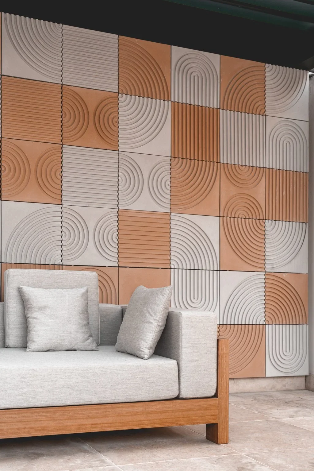 A beige sofa with two cushions in front of a textured wall with geometric patterns in earthy tones, arranged in a grid of 12 tiles.